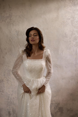 Close-up of the square neckline, beaded bodice, and sheer sparkly sleeves on an ivory wedding dress
