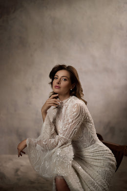 Ivory wedding dress with a high neckline, long sheer lace sleeves, and a draped tulle cape