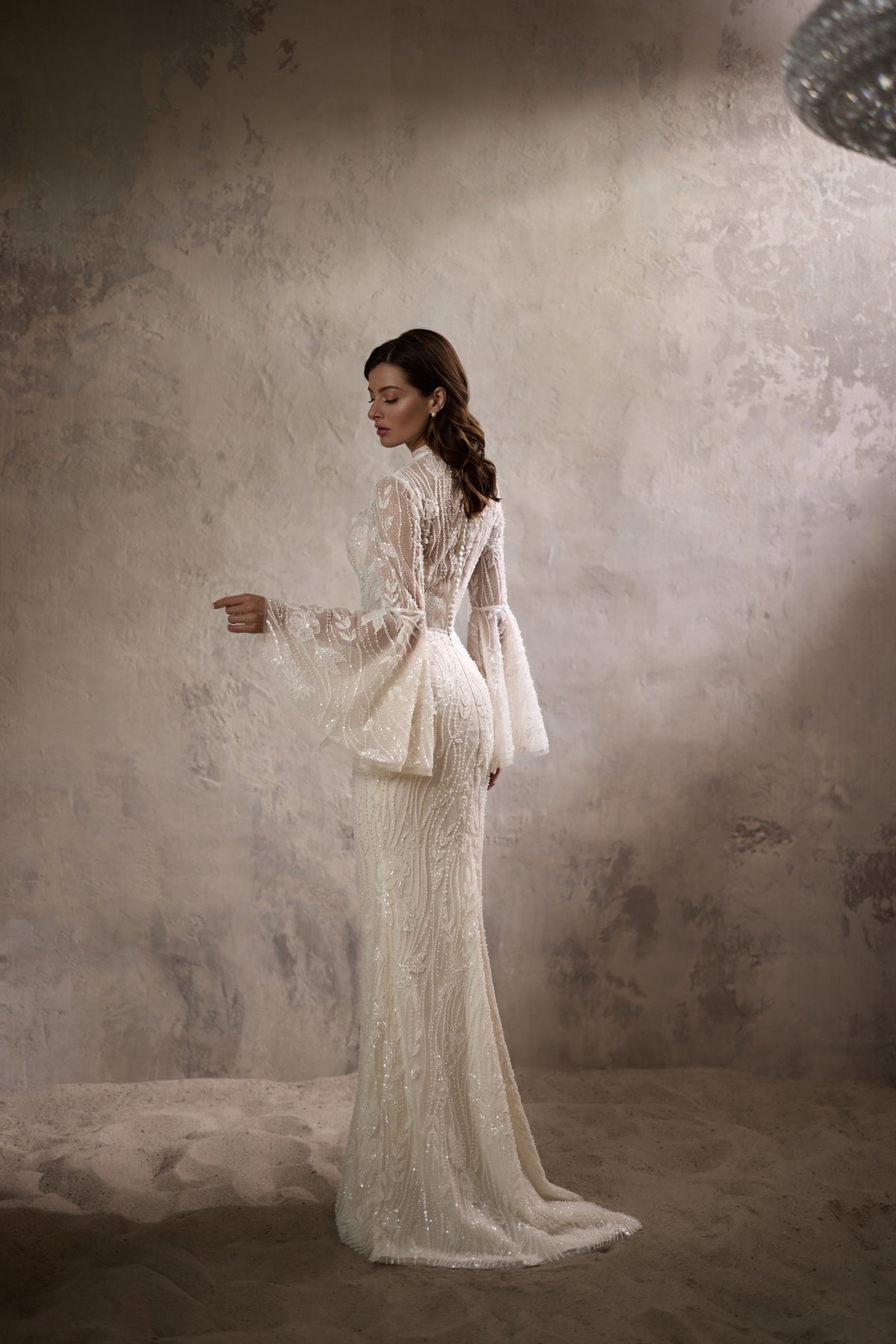 Side view of an ivory wedding dress with a sheer cape overlay, long sleeves, fitted skirt, and train