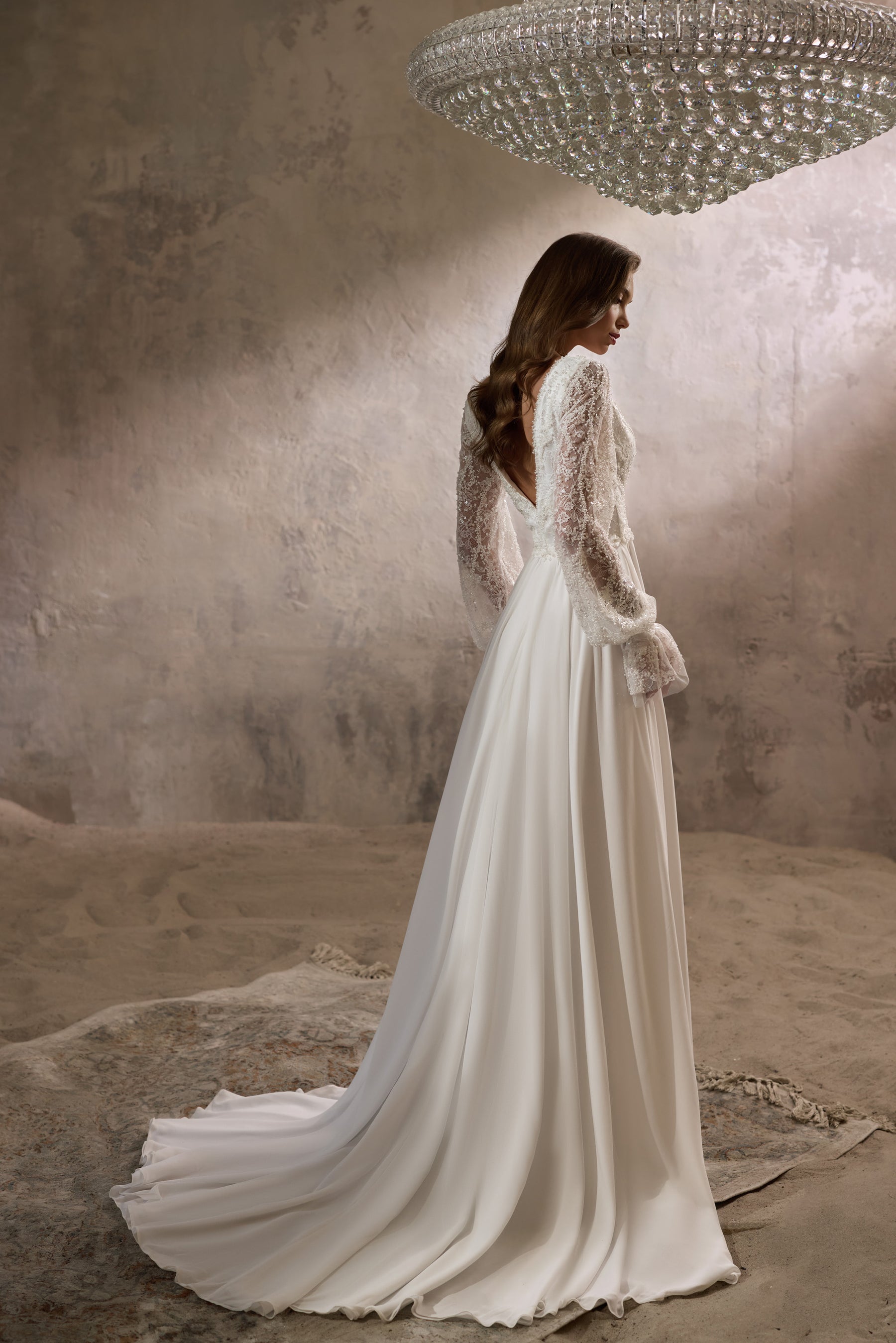 Ivory wedding dress with sheer lace long sleeves, flowing A-line skirt, and extended train shown from behind