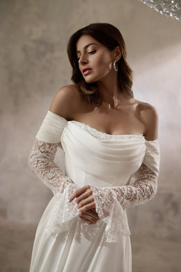 Close-up of an ivory wedding dress with a draped neckline, beaded trim, and floral lace sleeves