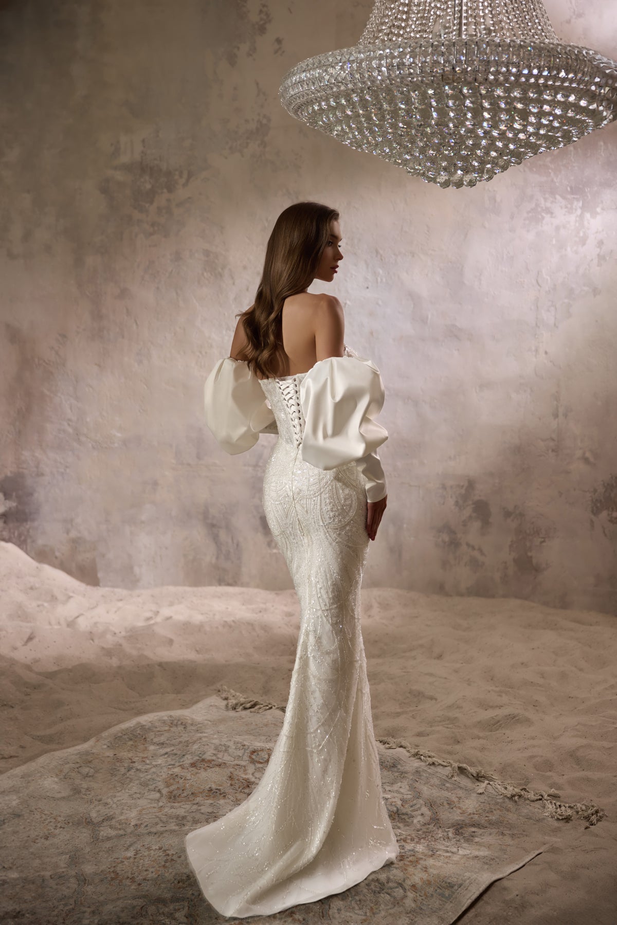 Back of an ivory beaded mermaid wedding dress with a low back, puff sleeves, and sweeping train