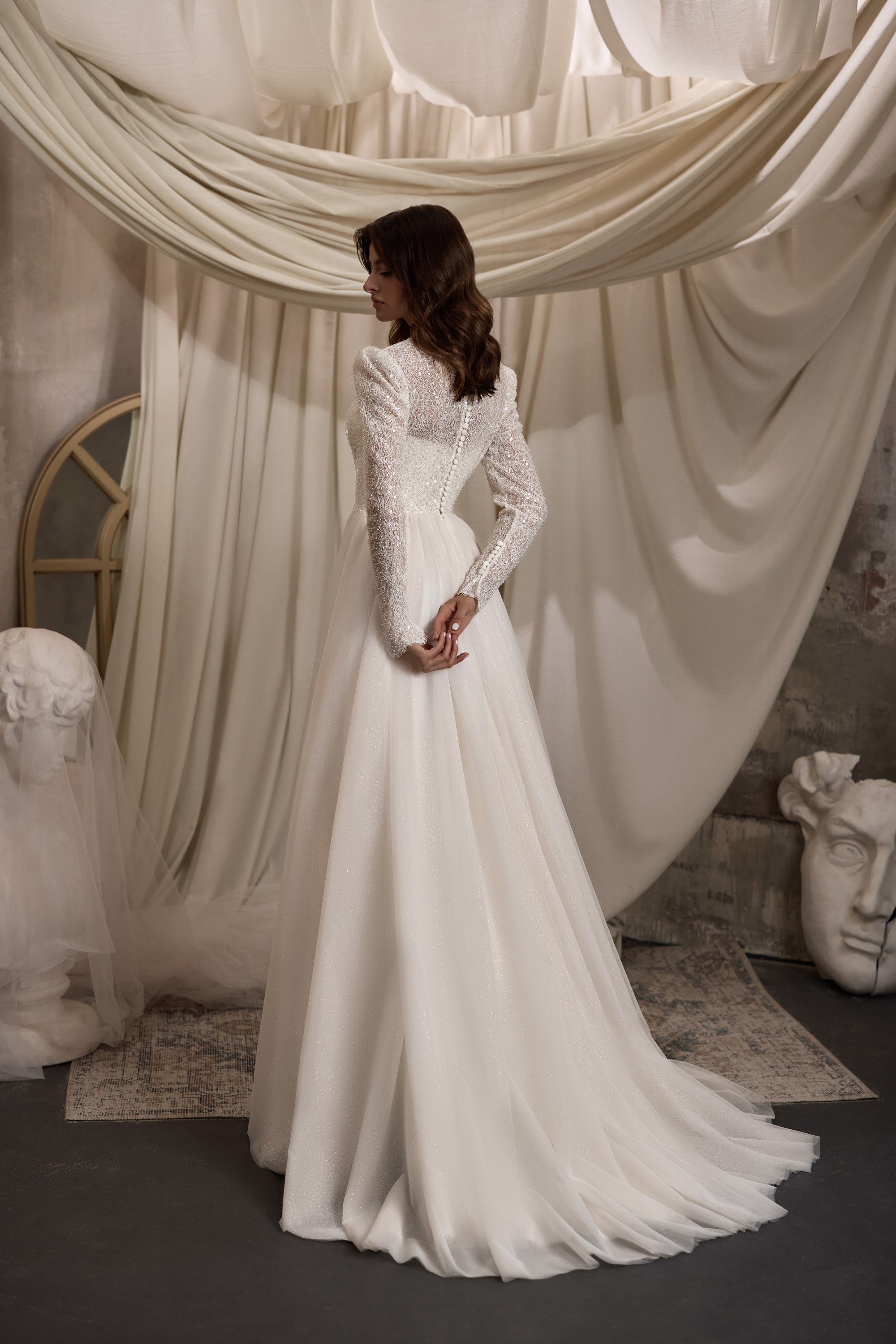 Ivory A-line wedding dress with sheer beaded lace long sleeves, high neck, and flowing train shown from behind