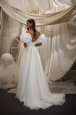 White wedding dress featuring puff sleeves, an open back, fitted waist, and flowing train