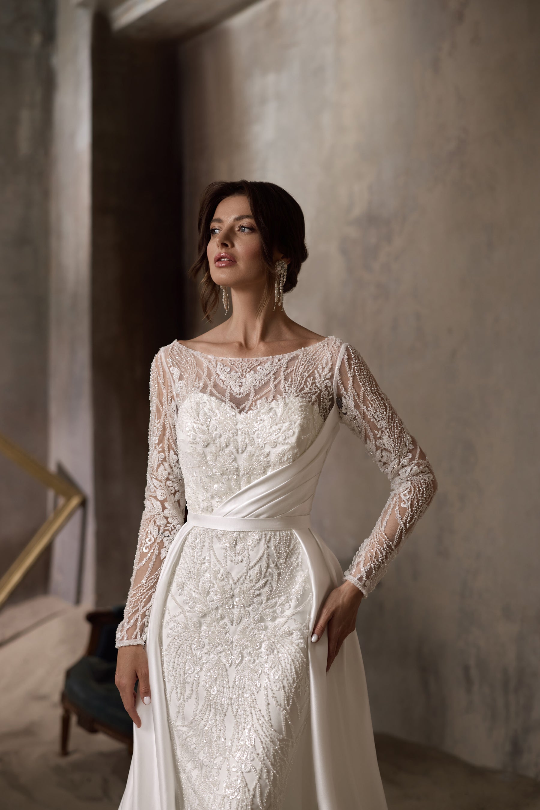 Close-up of an ivory wedding dress with floral lace, illusion sleeves, and a draped waist detail