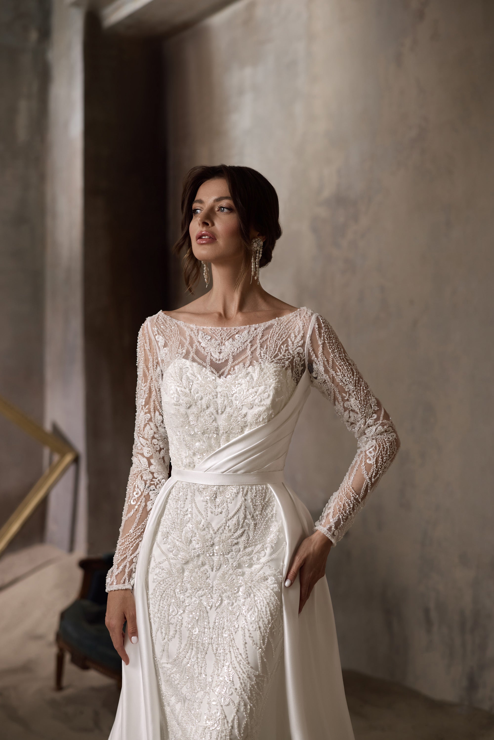 Close-up of an ivory wedding dress with floral lace, illusion sleeves, and a draped waist detail