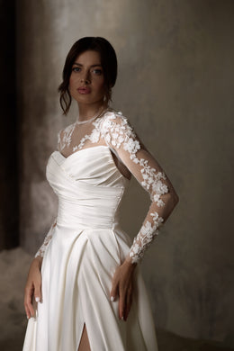 Close-up of an ivory wedding dress with ruched bodice and sheer floral lace sleeves