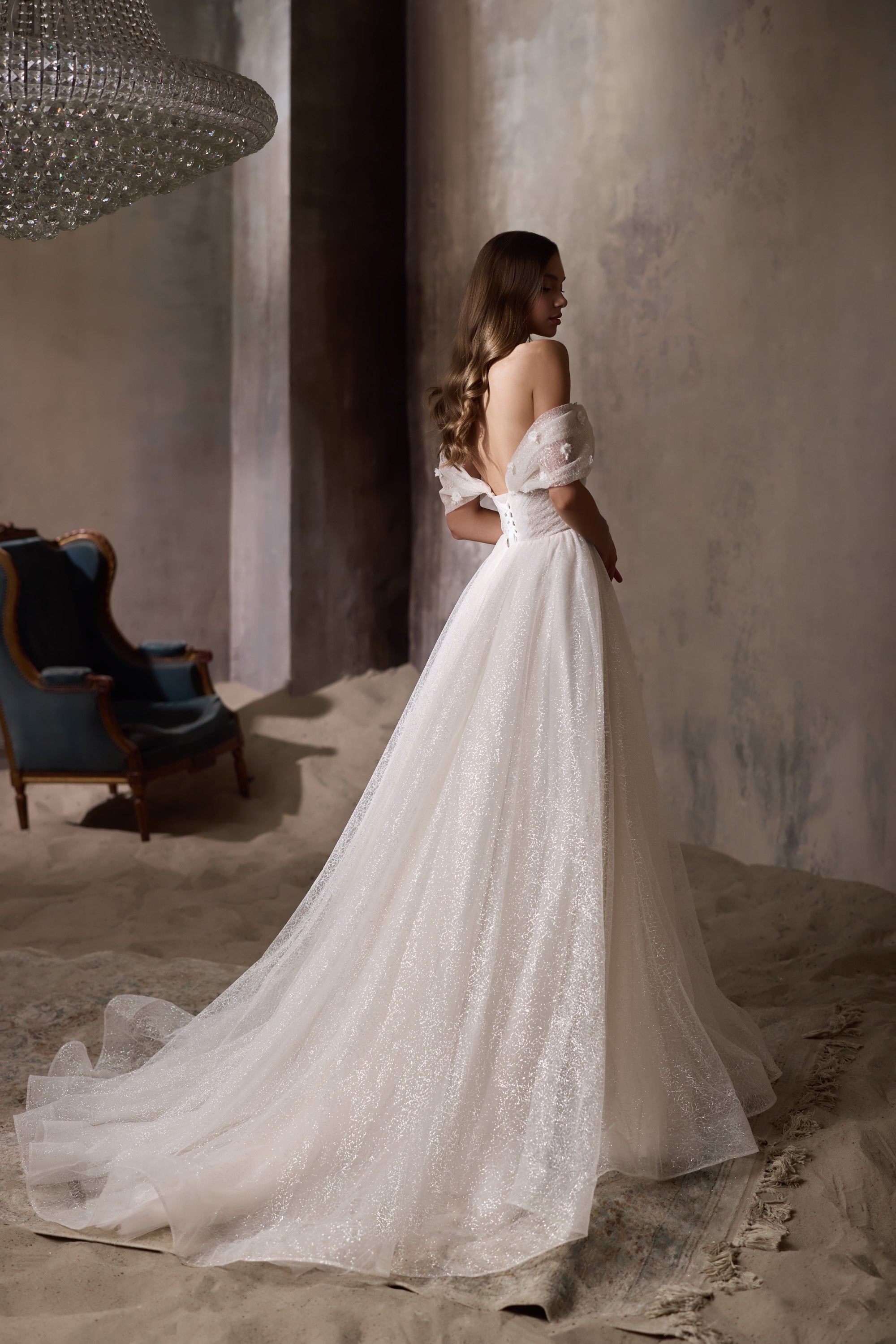 Back view of an ivory wedding dress with an open back, off-the-shoulder sleeves, glittering skirt, and train