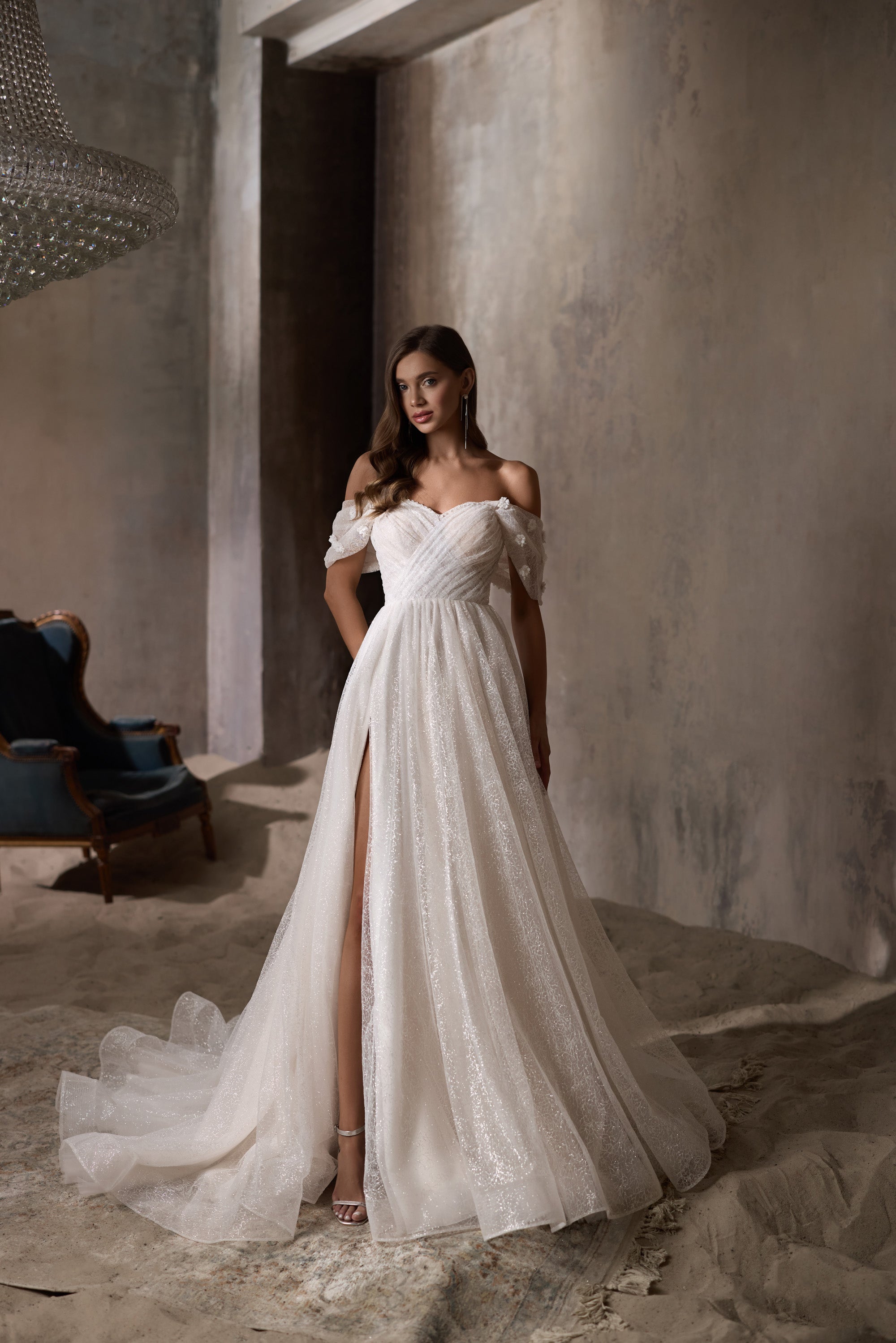 Ivory A-line wedding dress with an off-the-shoulder neckline, glittering tulle, thigh-high slit, and train