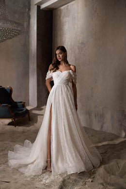 Ivory A-line wedding dress with an off-the-shoulder neckline, glittering tulle, thigh-high slit, and train