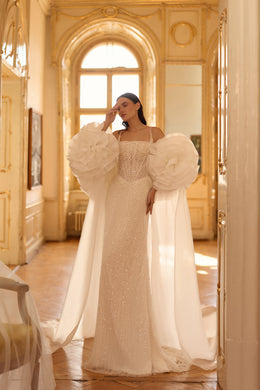 Beaded ivory wedding dress paired with a flowing cape and oversized floral shoulder details