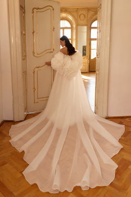 Flowing cape and cathedral-length train drape behind an ivory wedding dress
