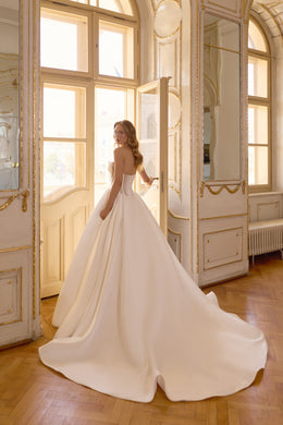 Open-back ivory wedding dress with off-the-shoulder sleeves, a full ball-gown skirt, and a broad trailing train