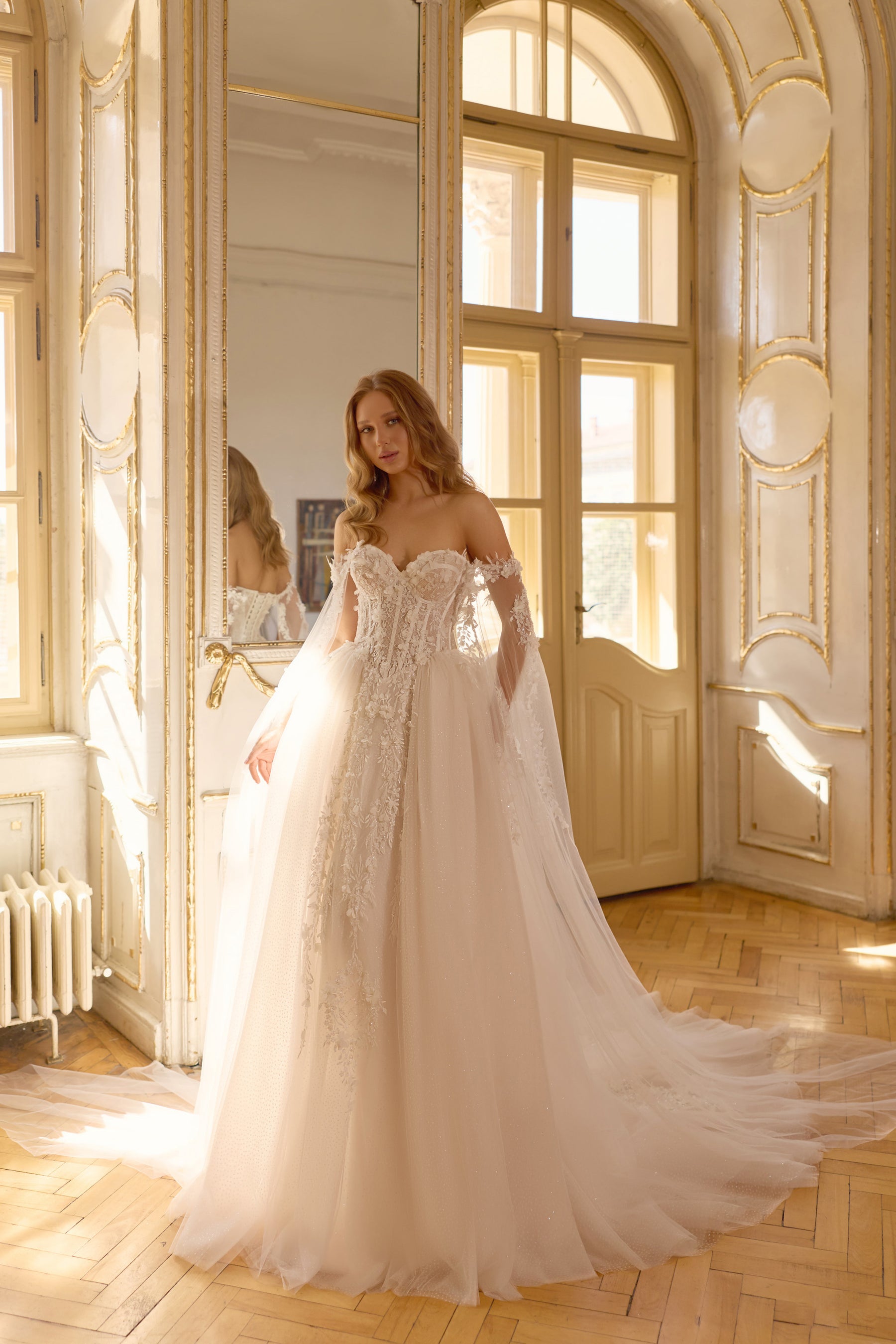 Ivory ball gown wedding dress with an off-the-shoulder lace bodice, sheer sleeves, and a flowing train