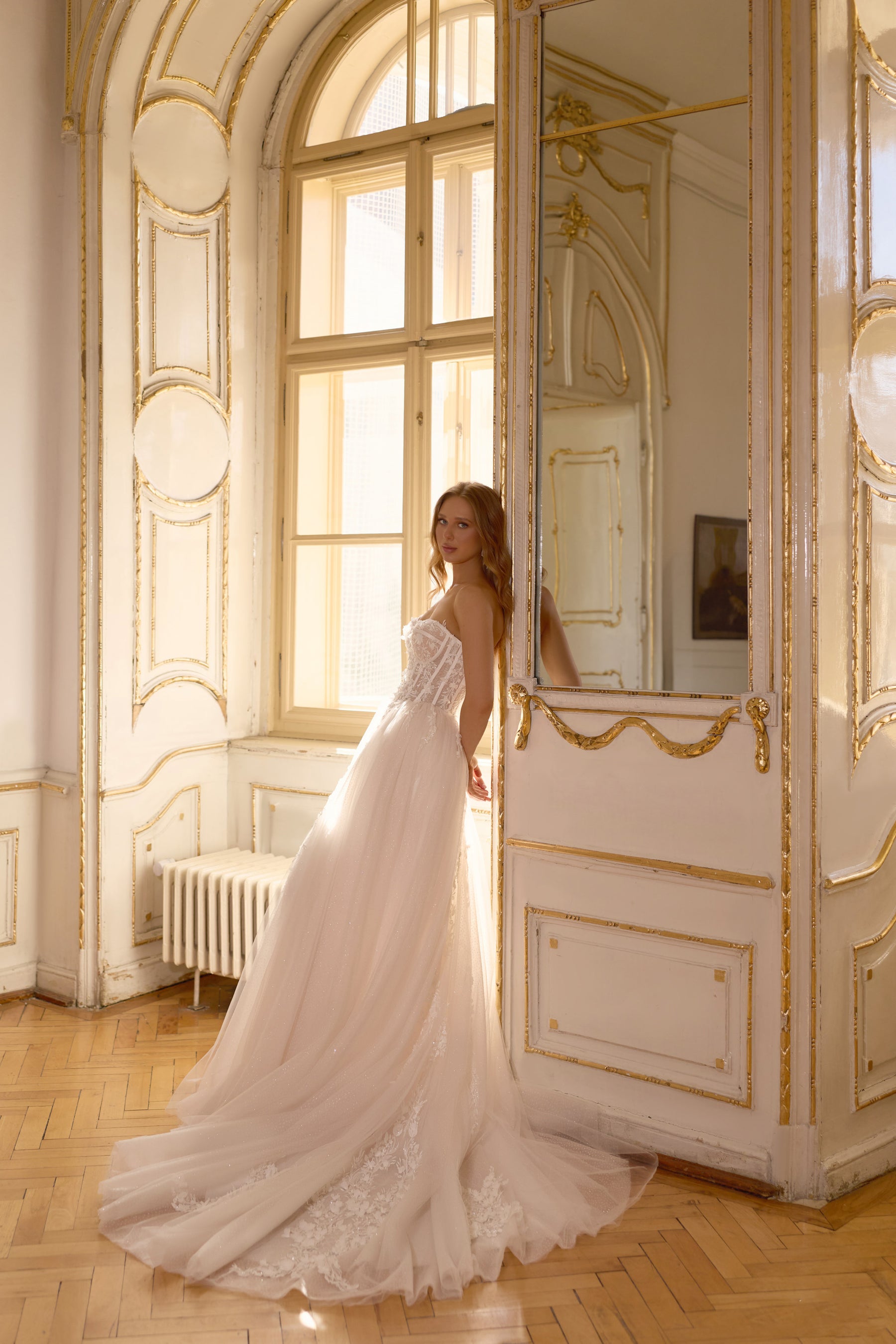 Side silhouette of an ivory ball gown wedding dress with a sweeping tulle train and floral lace hem