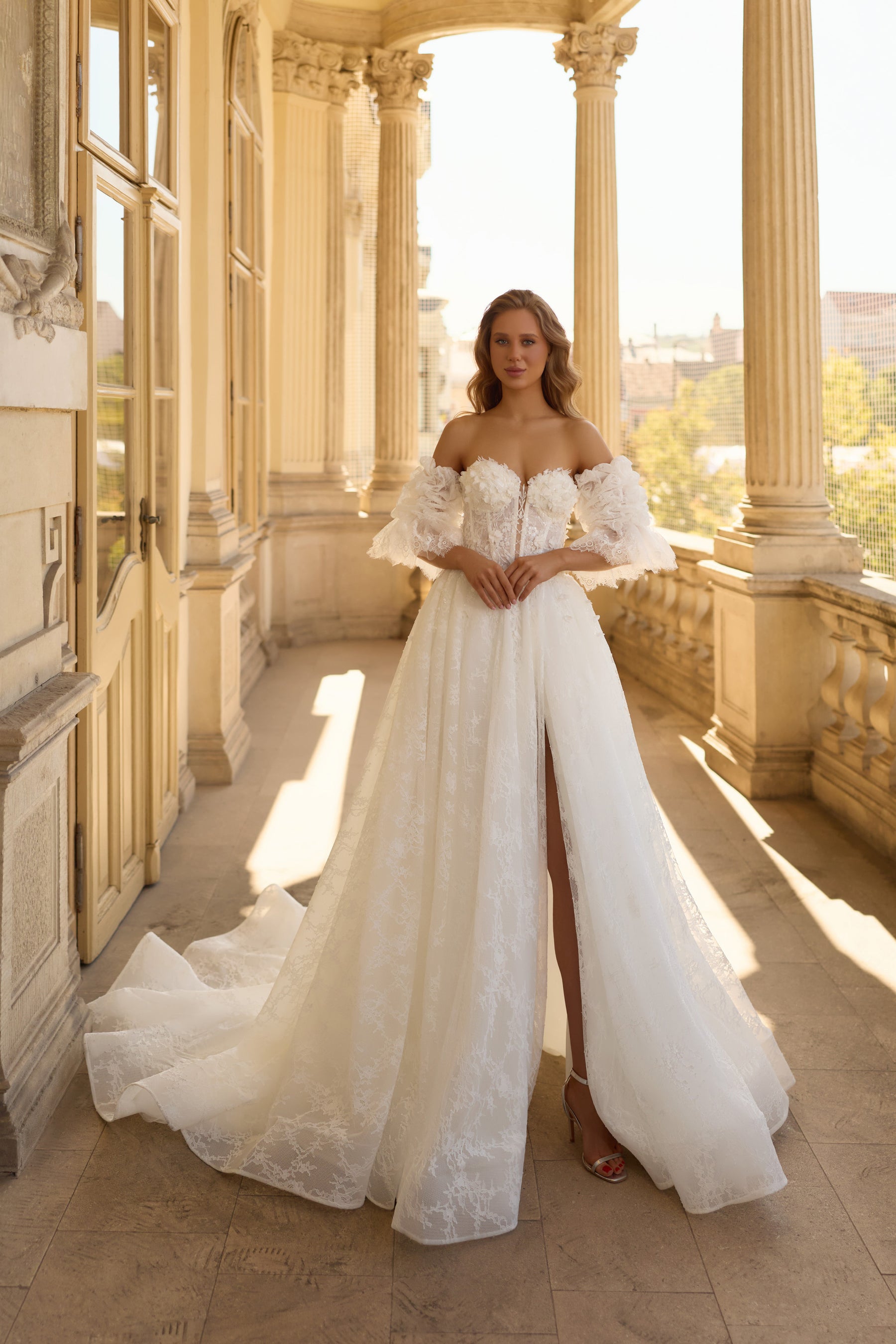 Ivory A-line wedding dress with an off-the-shoulder neckline, lace puff sleeves, high slit, and long train