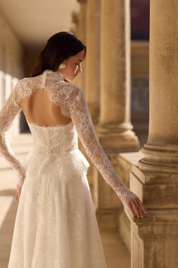 Open-back ivory wedding dress framed by floral lace sleeves, with a fitted waist and flowing skirt