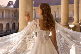 Lace-up corset back and sheer cape sleeves on an ivory wedding dress with a flowing train