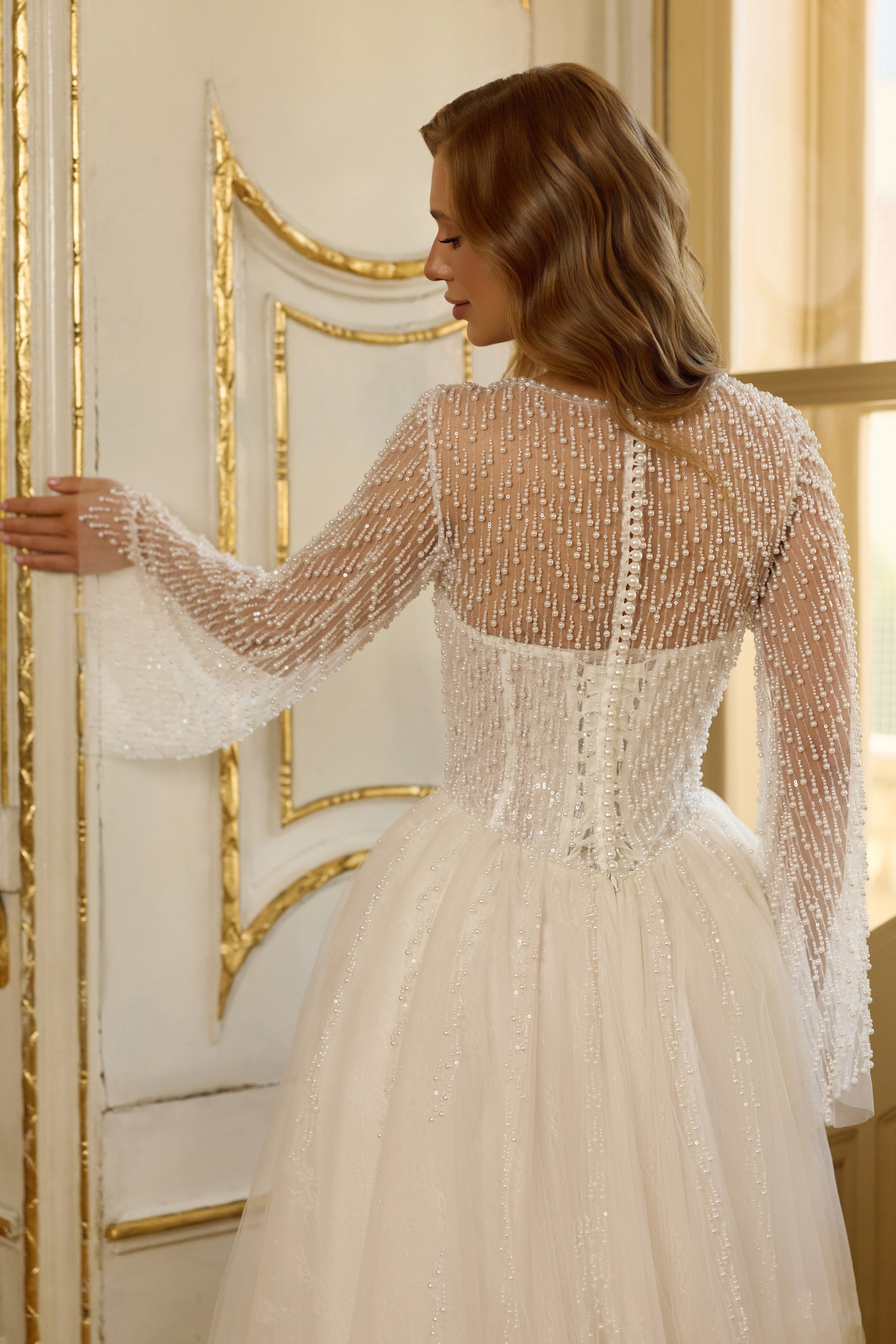 Close-up of the sheer beaded back, long sleeves, and fitted waist on a wedding dress