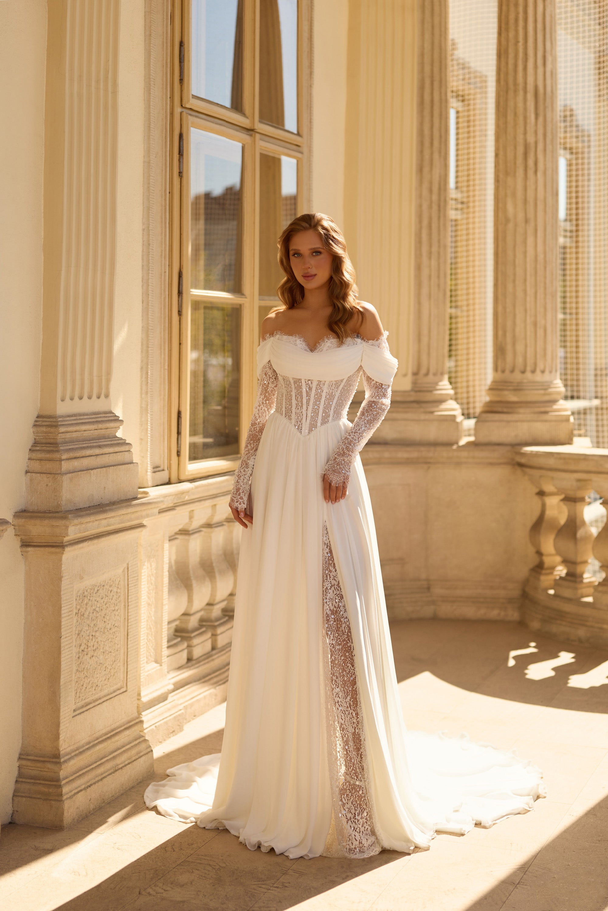 Ivory wedding dress with an off-the-shoulder neckline, sheer lace sleeves, beaded corset, and flowing train