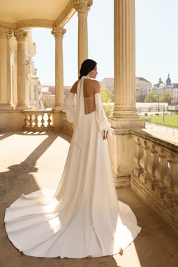 Open-back ivory wedding dress with corset-style straps, flowing skirt, and an extended train