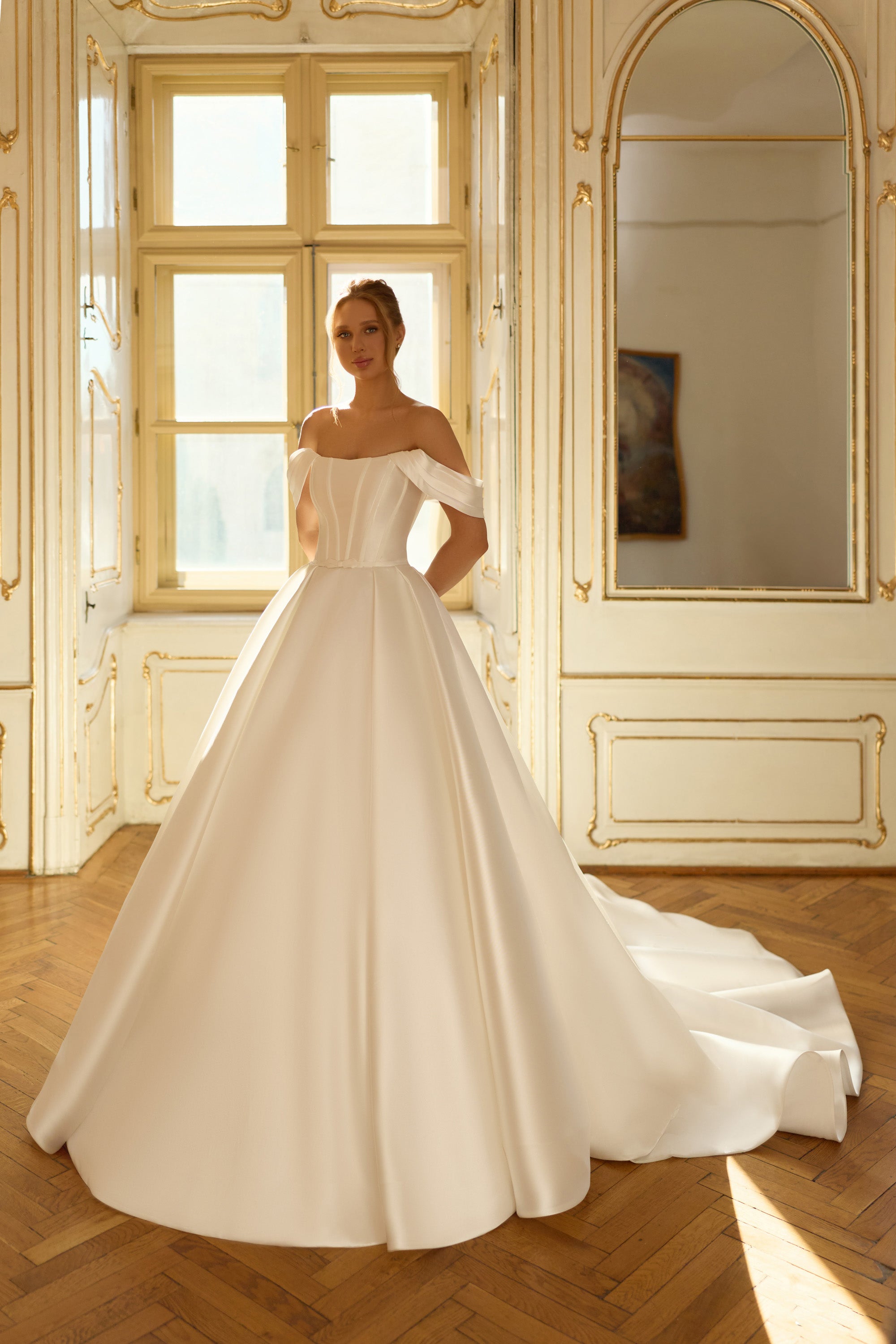 Ivory satin ball gown wedding dress with an off-the-shoulder neckline, fitted bodice, and sweeping train