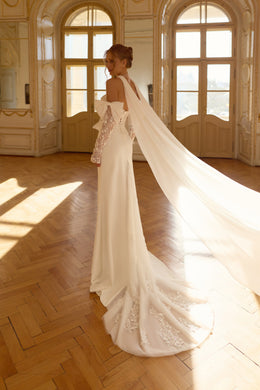 Side-back view of an ivory wedding dress with lace sleeves, a flowing cape, and floral lace-trimmed train