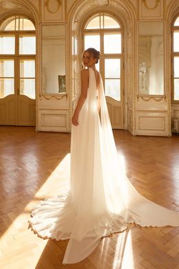 Back of an ivory wedding dress with a long flowing cape and wide scalloped train