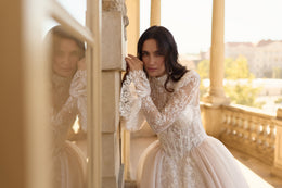 Close-up of an ivory wedding dress with floral lace bodice, high neckline, sheer long sleeves, and full skirt