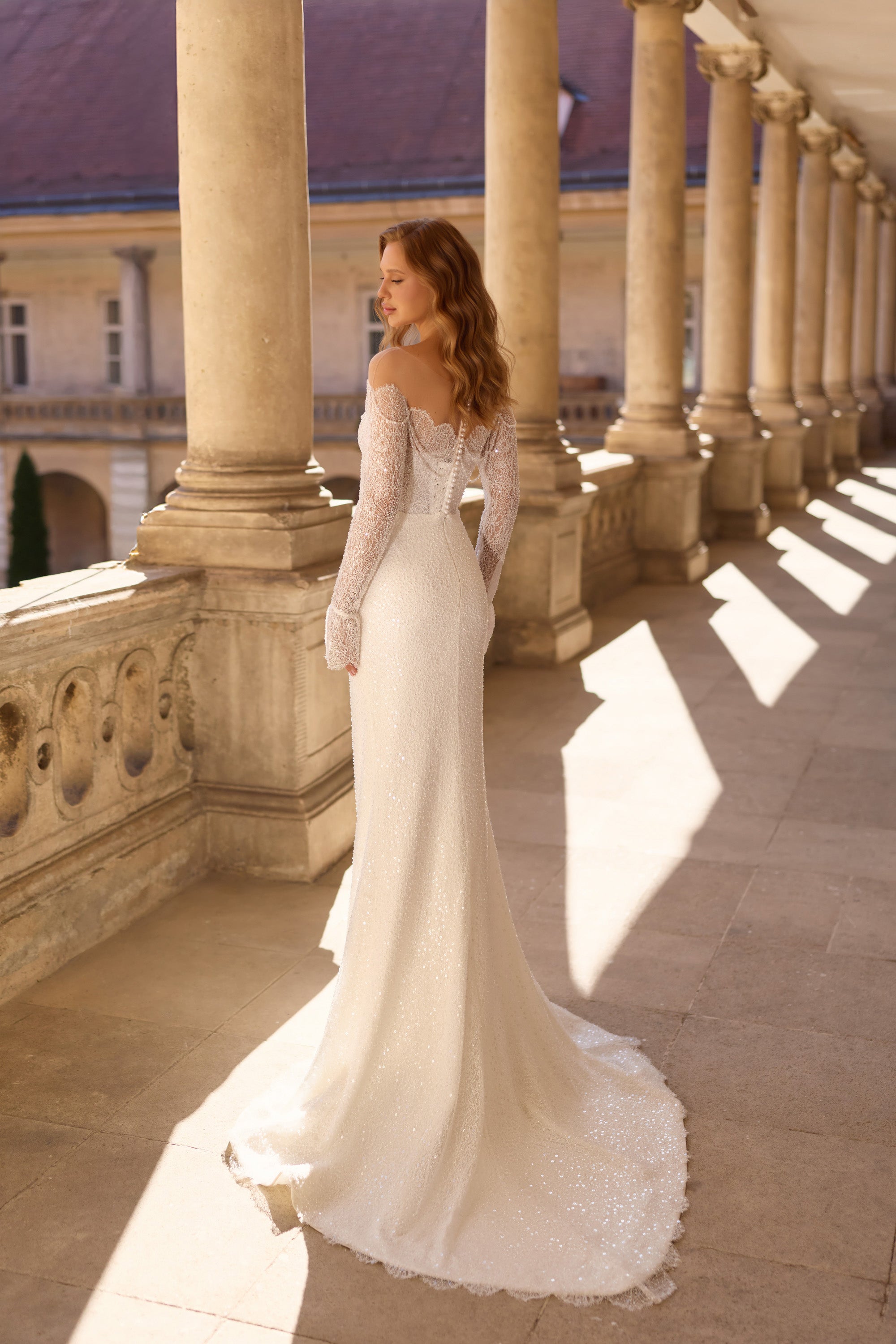 Three-quarter back view of an ivory wedding dress with sheer beaded sleeves and a sweeping train