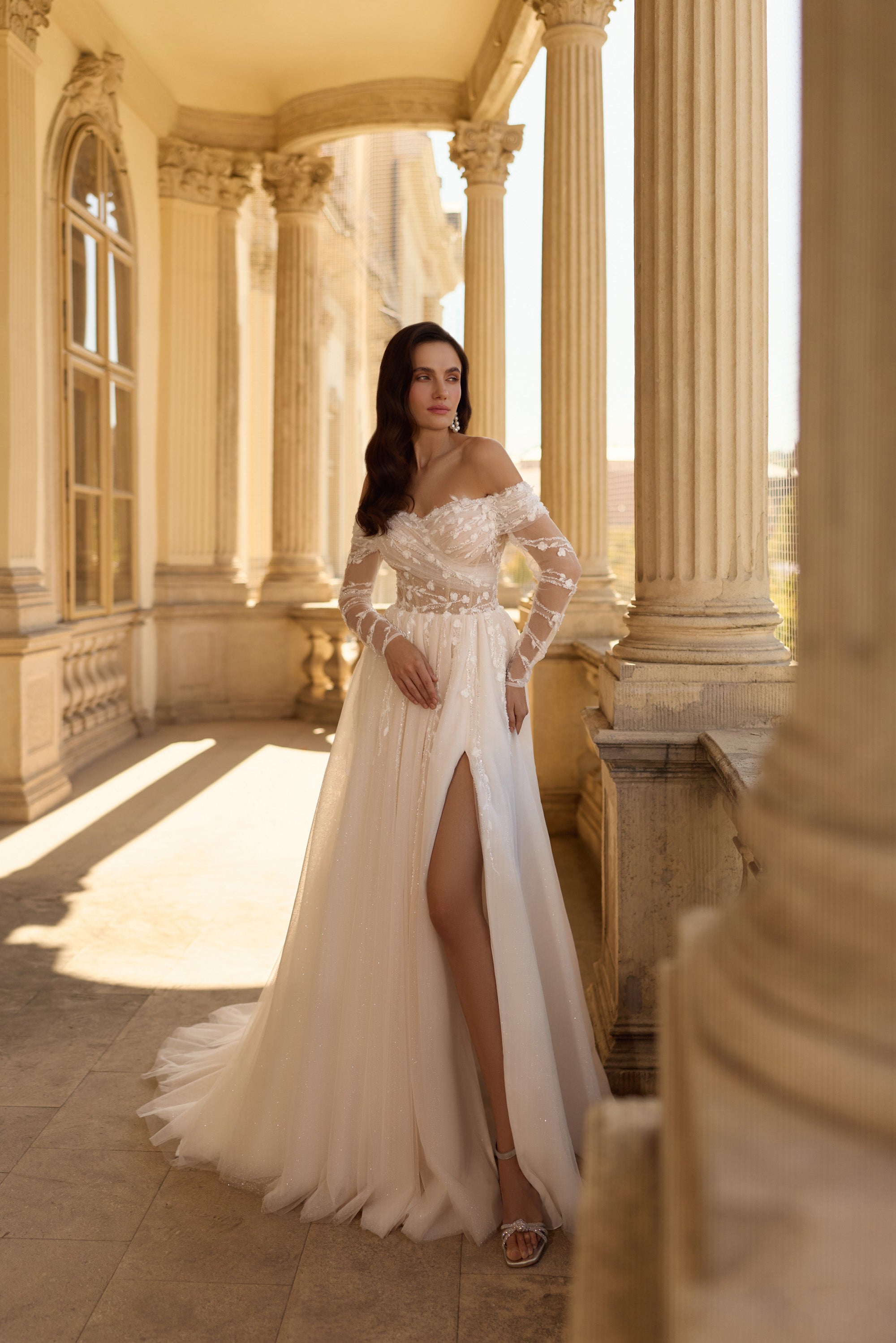 Ivory A-line wedding dress with an off-the-shoulder neckline, floral lace sleeves, slit, and train