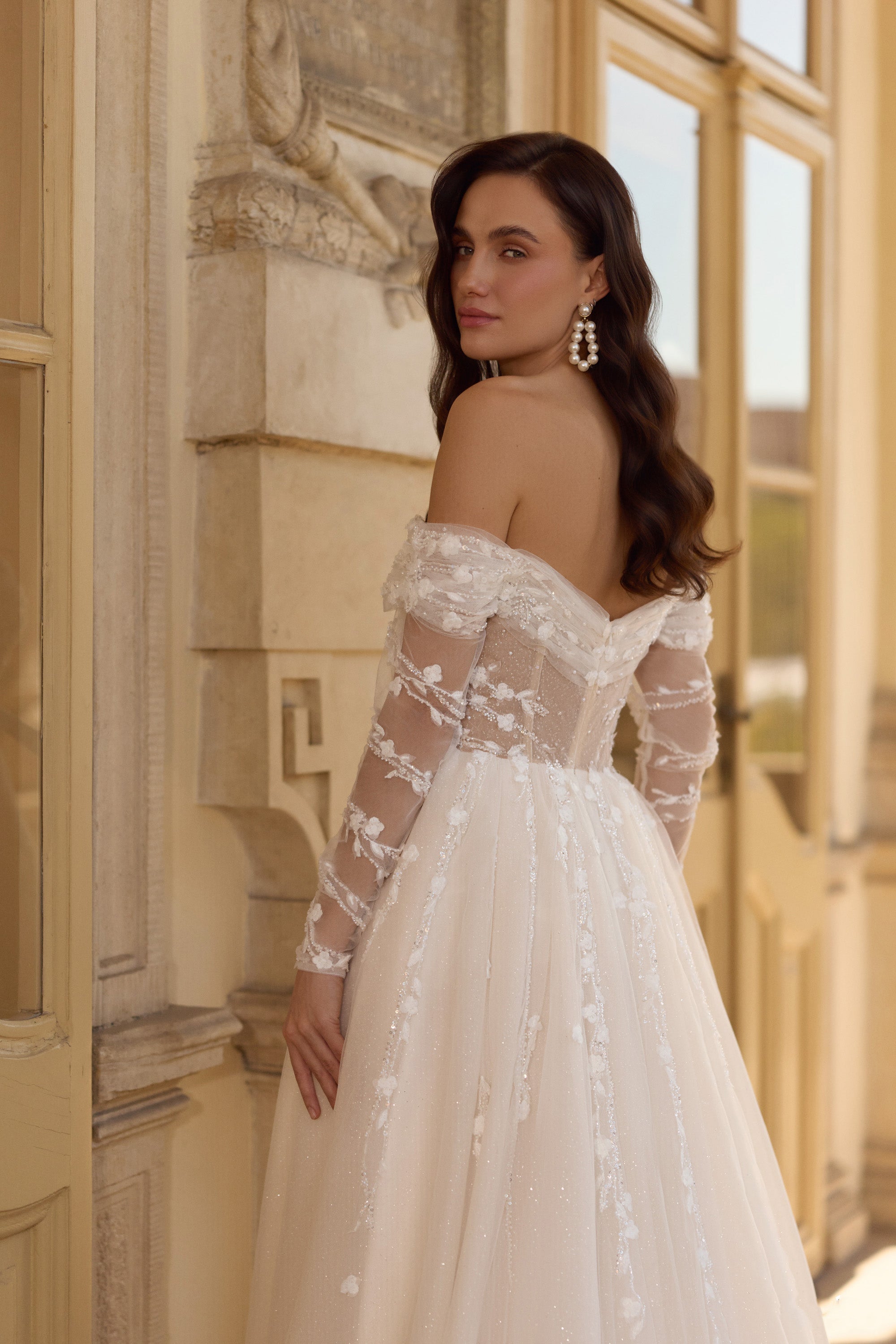 Three-quarter back view of an ivory wedding dress with sheer floral lace sleeves and a low open back