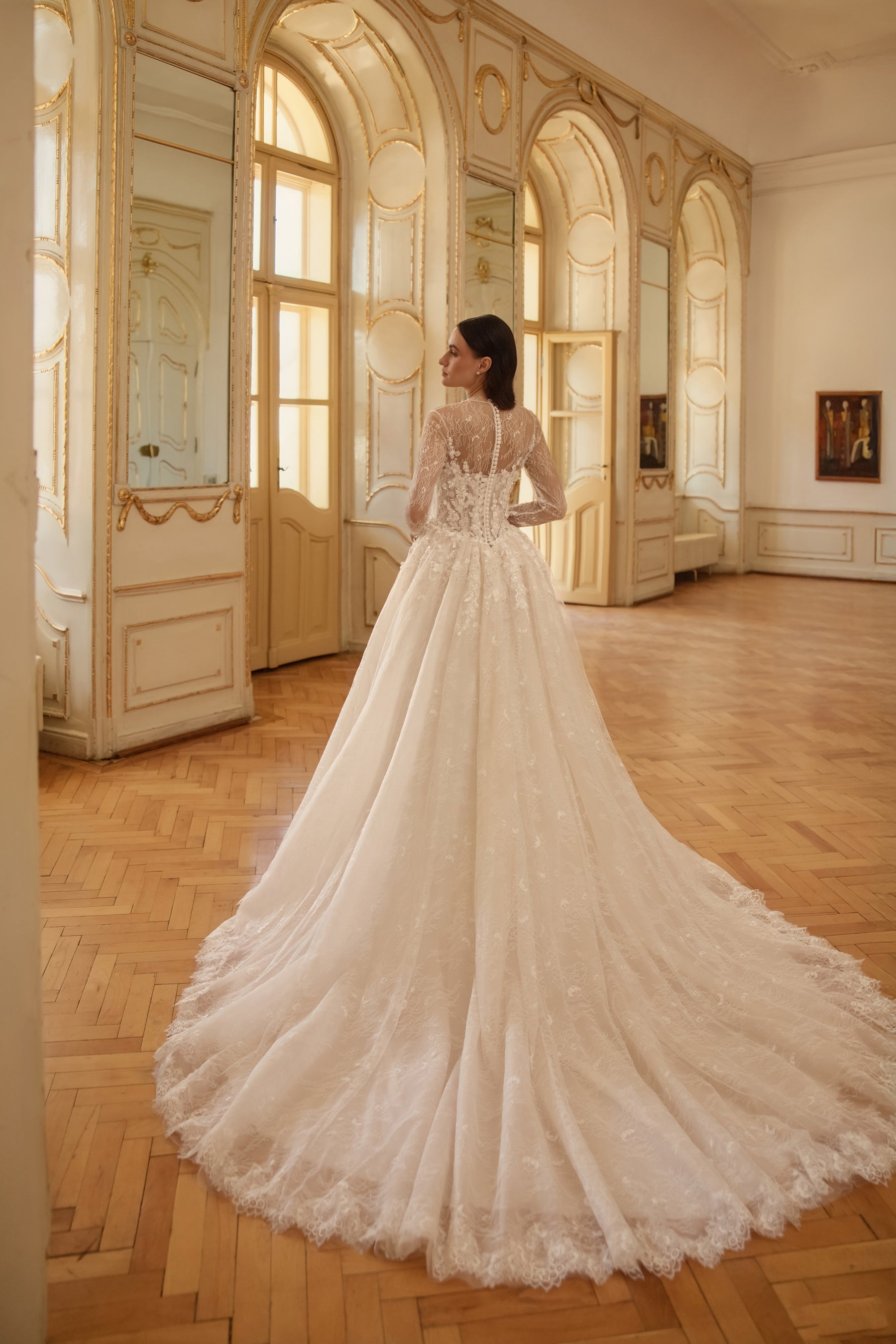 Lace-backed ivory wedding dress with sheer long sleeves, a full skirt, and an extended train