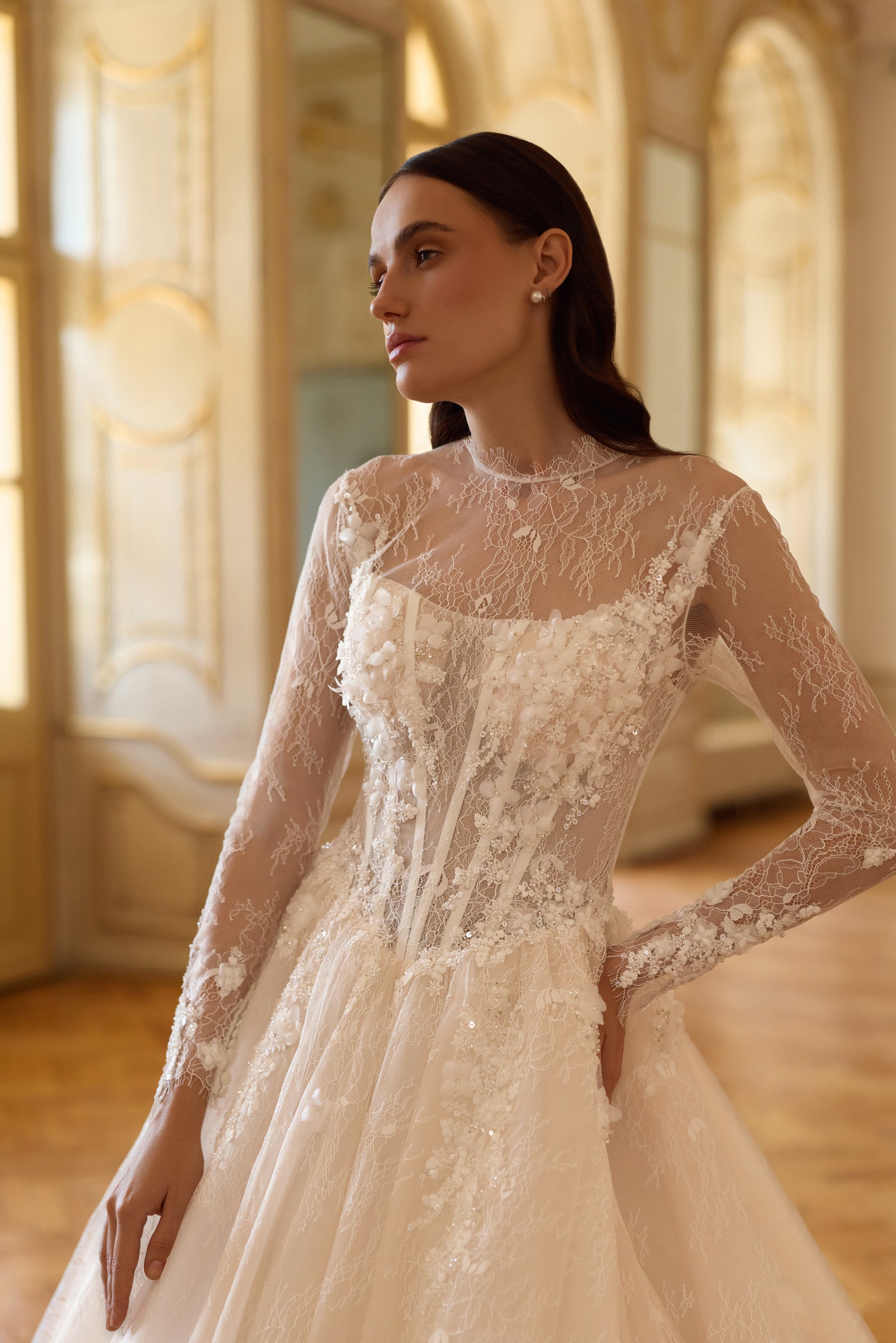 Close-up of an ivory wedding dress bodice with floral lace, sheer sleeves, and a high illusion neckline
