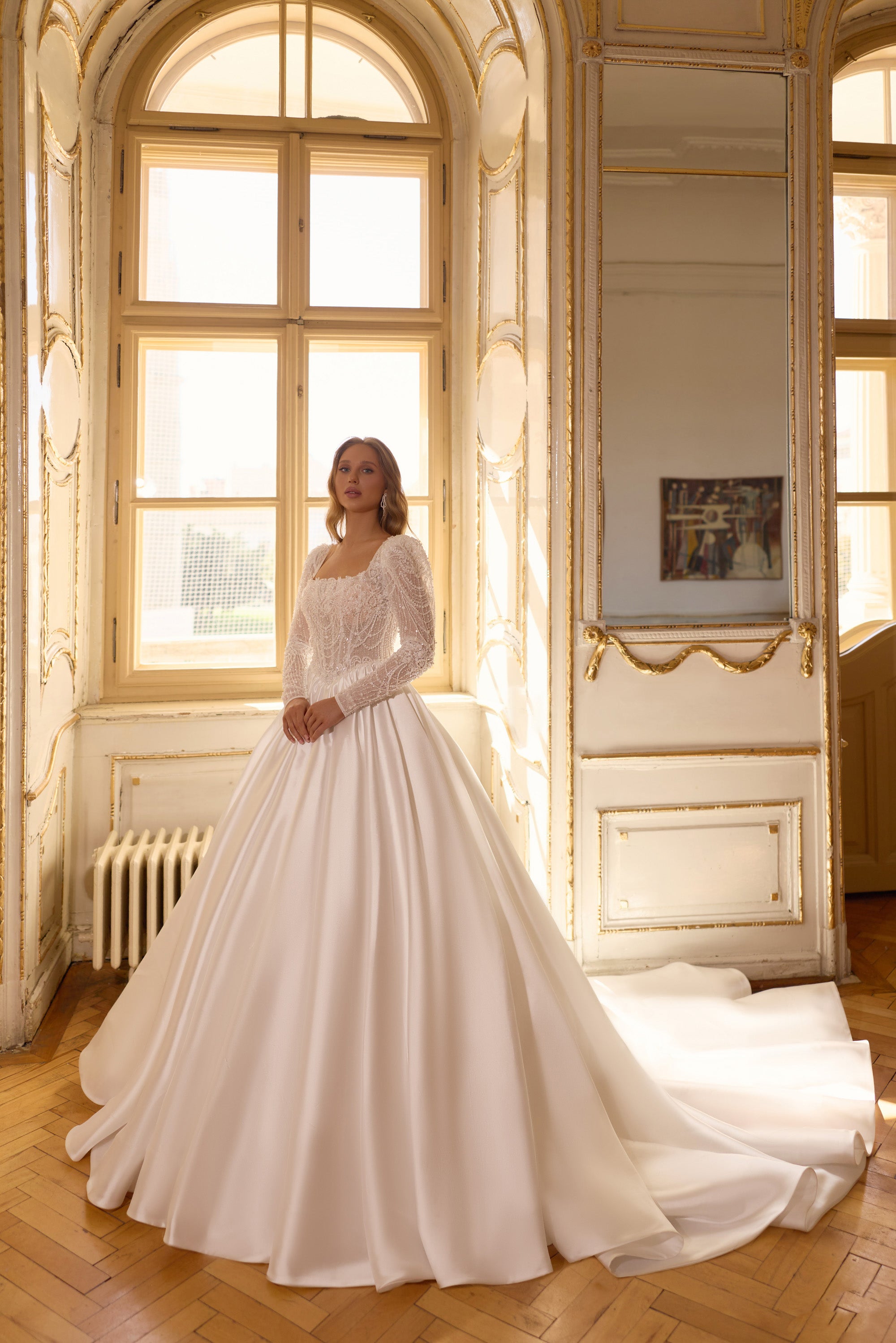 Ivory ball gown wedding dress with a beaded bodice, long sheer sleeves, and a full satin skirt