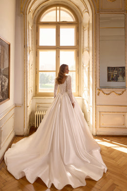 Ivory wedding dress with a full pleated skirt, long sleeves, and a sweeping train seen from the back