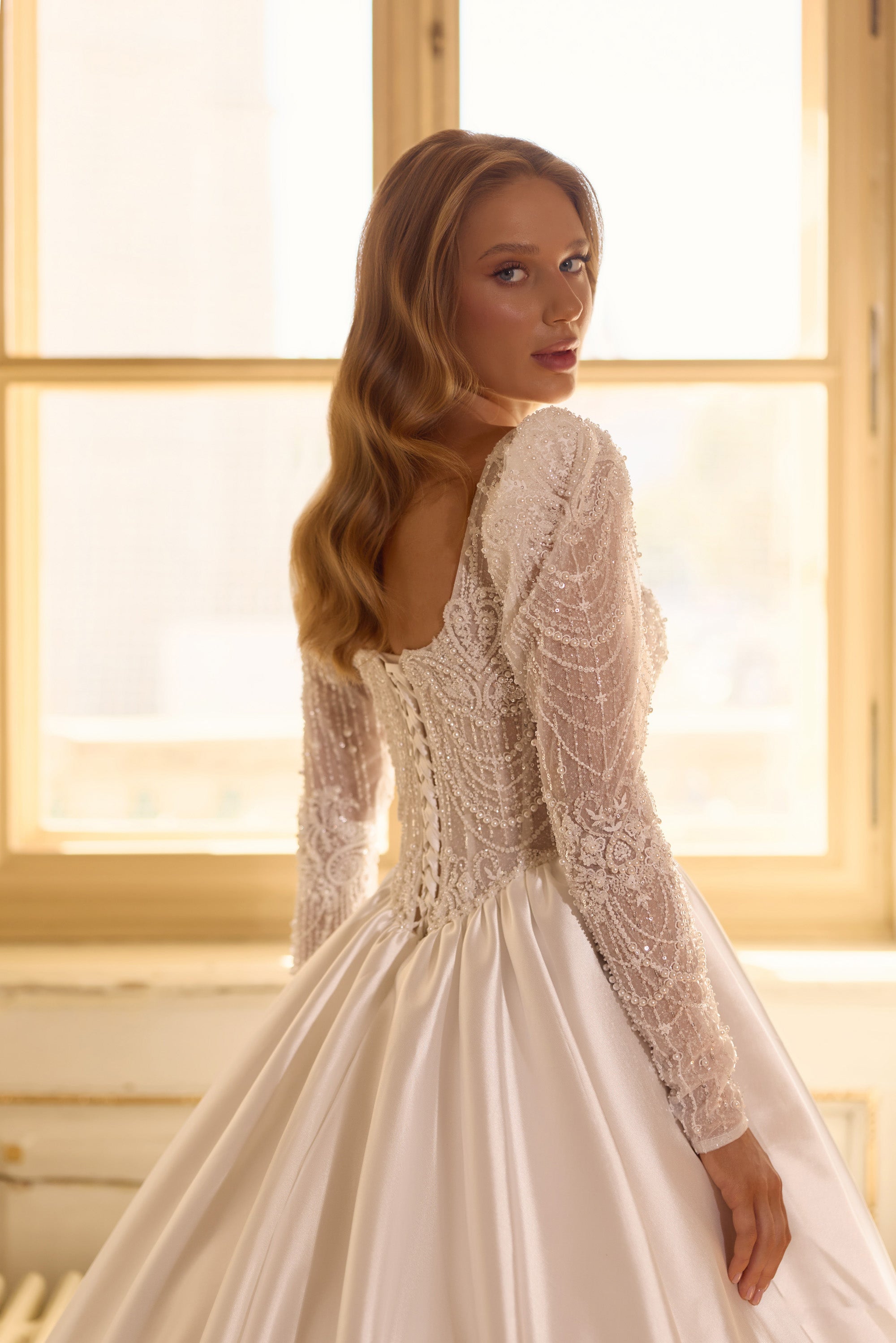 Close-up of an open square back, beaded long sleeves, and gathered waist on an ivory wedding dress