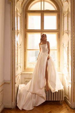 Ivory wedding dress with a beaded square neckline, thigh-high slit, and flowing overskirt