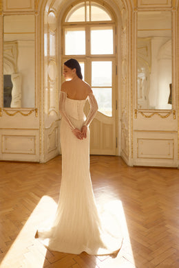 Beaded mermaid wedding dress showing its off-the-shoulder back, long sleeves, and flared train
