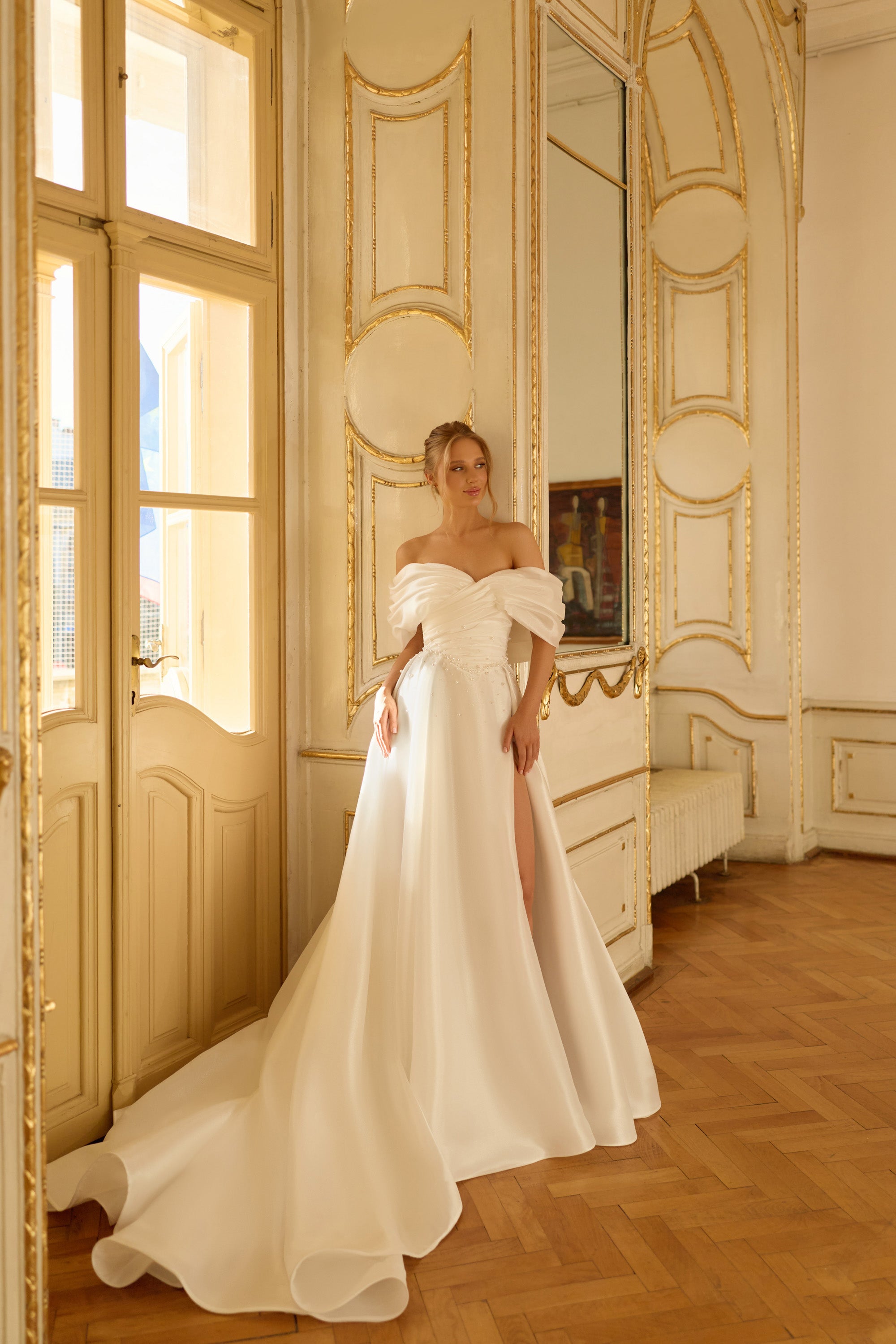 Draped off-the-shoulder ivory wedding dress with a flowing A-line skirt, slit, and long train