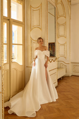 Draped off-the-shoulder ivory wedding dress with a flowing A-line skirt, slit, and long train