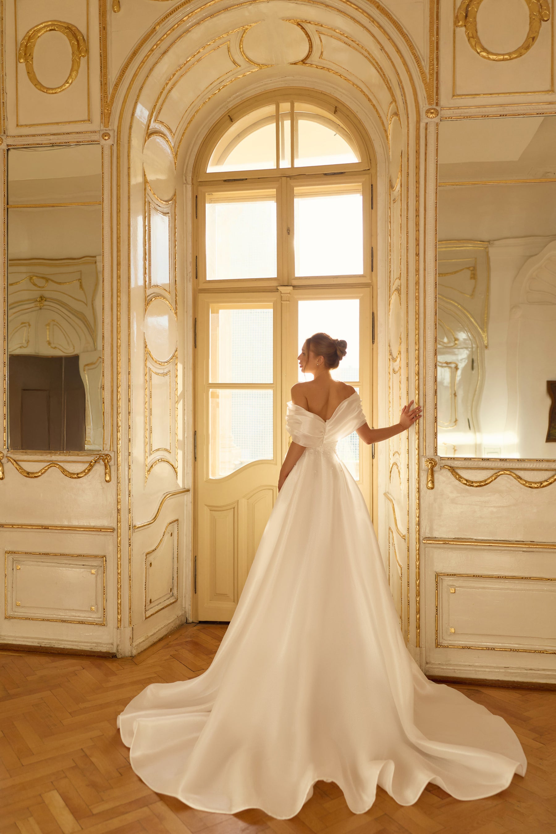 Rear view of an ivory off-the-shoulder wedding dress with a full flowing skirt and long train
