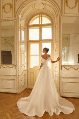 Rear view of an ivory off-the-shoulder wedding dress with a full flowing skirt and long train