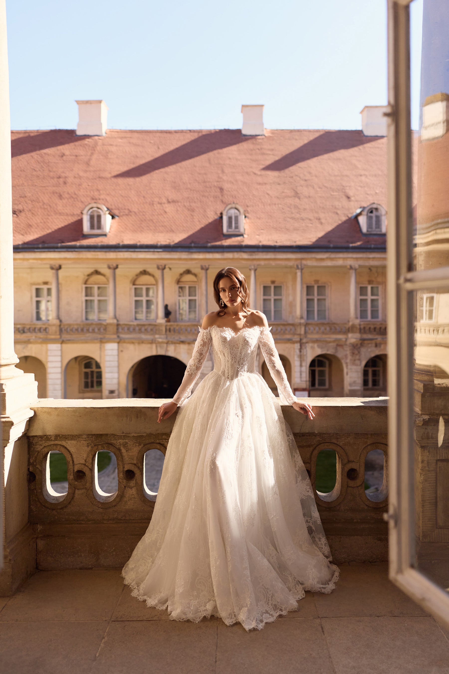 Full-length ivory wedding dress with long lace sleeves, floral detailing, and a sweeping A-line skirt