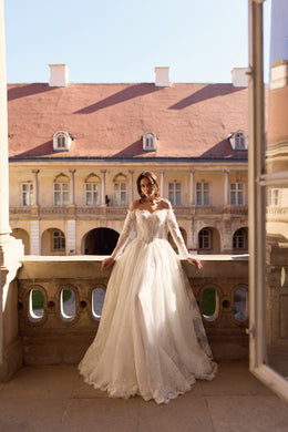 Full-length ivory wedding dress with long lace sleeves, floral detailing, and a sweeping A-line skirt