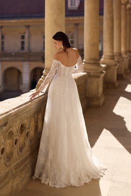 Open-back ivory wedding dress with lace sleeves, floral texture, and a long flowing train