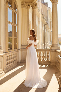 Flowing white wedding dress with an off-the-shoulder floral ruffle neckline and sweeping train, shown from behind