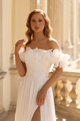 Close-up of an off-the-shoulder white wedding dress with layered floral ruffles and a pleated bodice