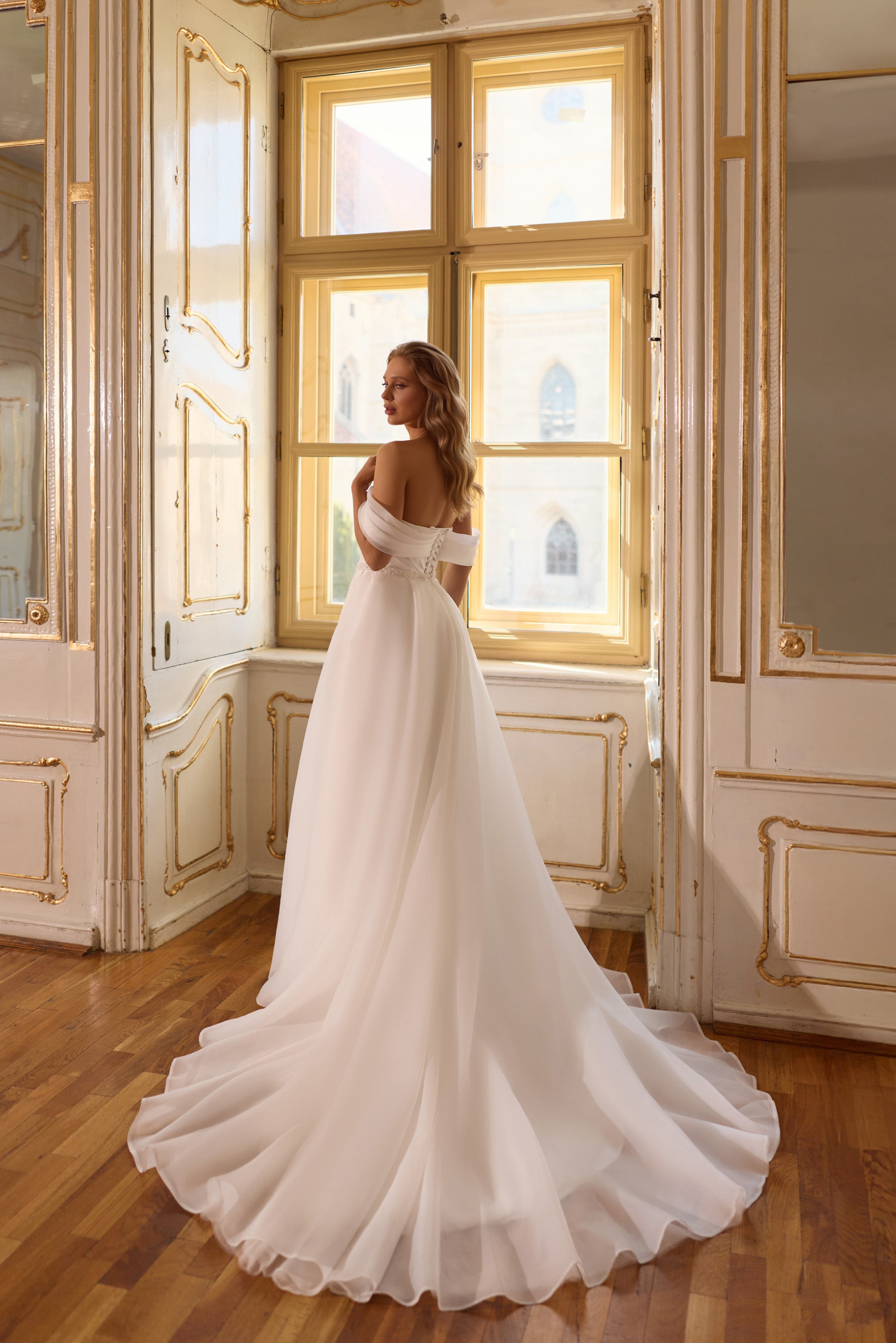 Side view of an ivory wedding dress with an off-the-shoulder neckline, bare upper back, and flowing train