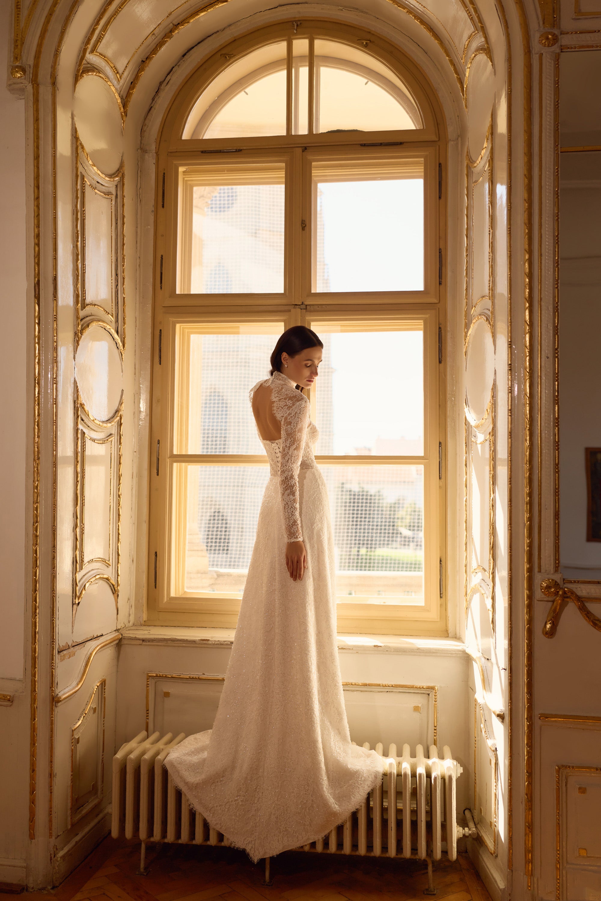 Side view of an ivory lace wedding dress with long sleeves, fitted sheath silhouette, and sweeping train